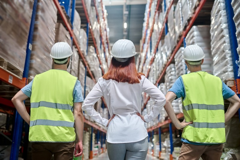 3 Arbeiter stehen vor Regalen in einer Lagerhalle